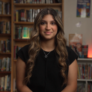 Atriya Nourbakhsh sitting in front of a library of books.